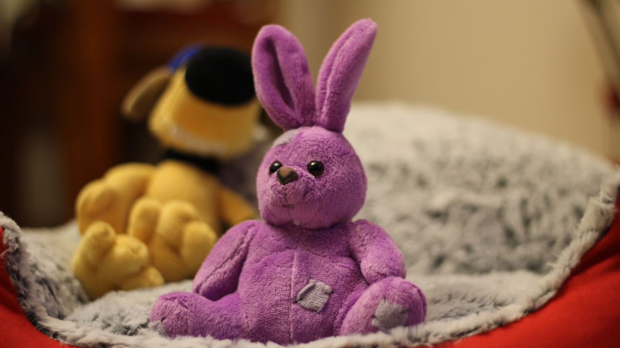 Old, pink stuffed animal bunny sitting on bed