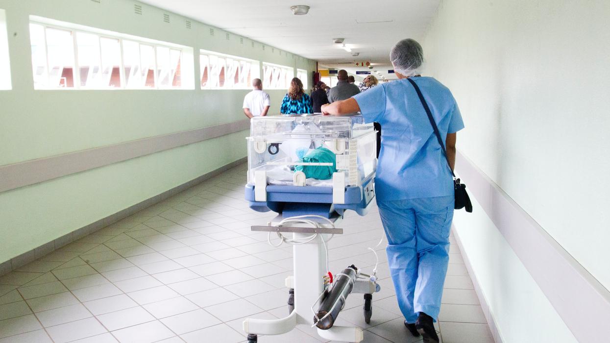 Orderly walking an incubator down a hospital corridor.