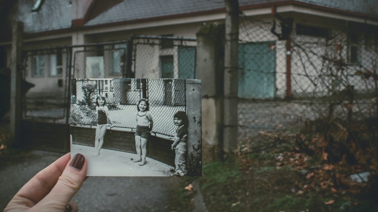 person holding photo of three girls near chainlink fence