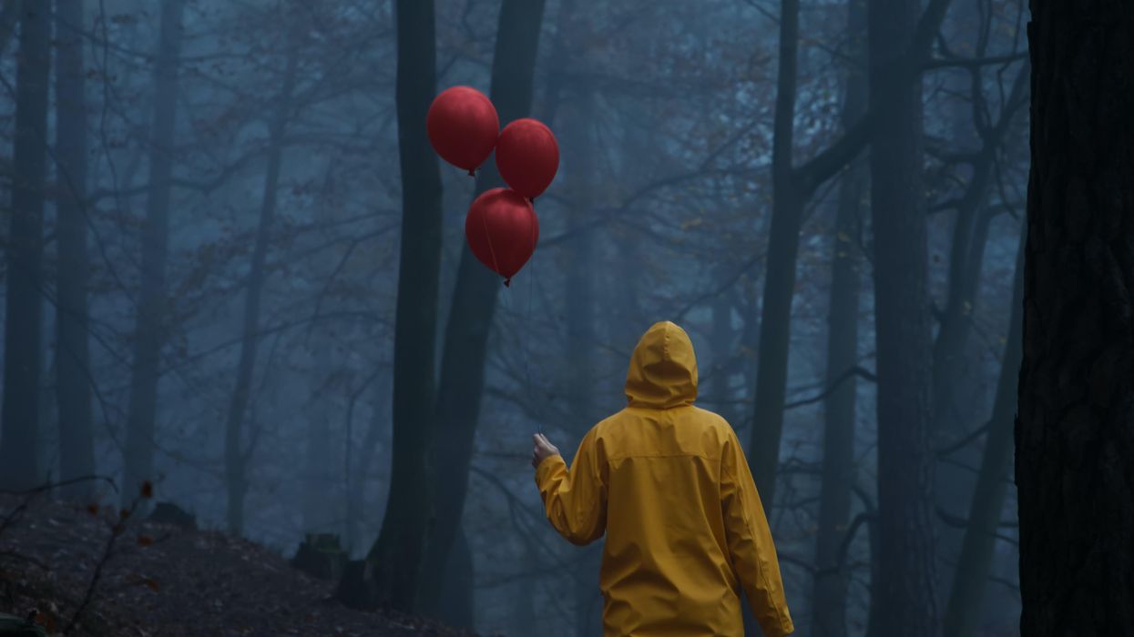 Person holding red balloons in a dark forest