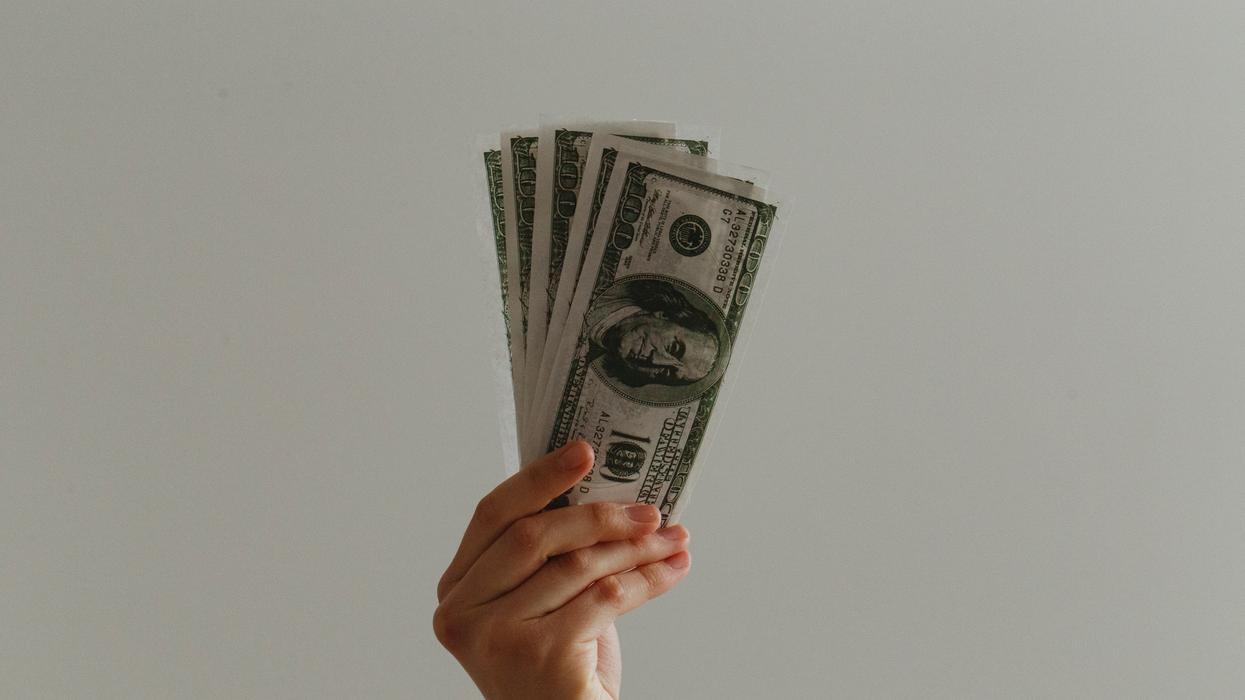 Person holding up multiple $100 U.S. dollar bills