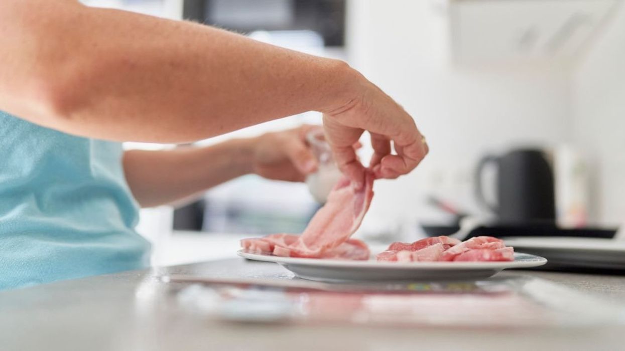 Person in the kitchen handling uncooked slices of pork