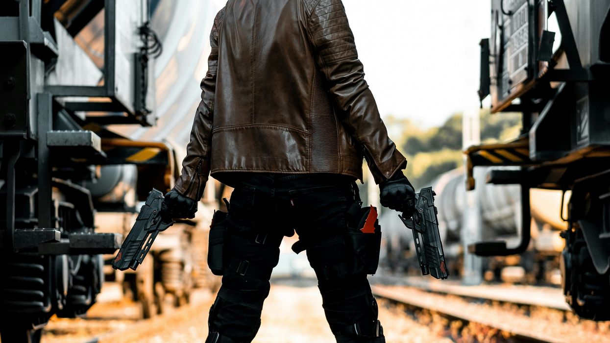 person in train yard holding two guns