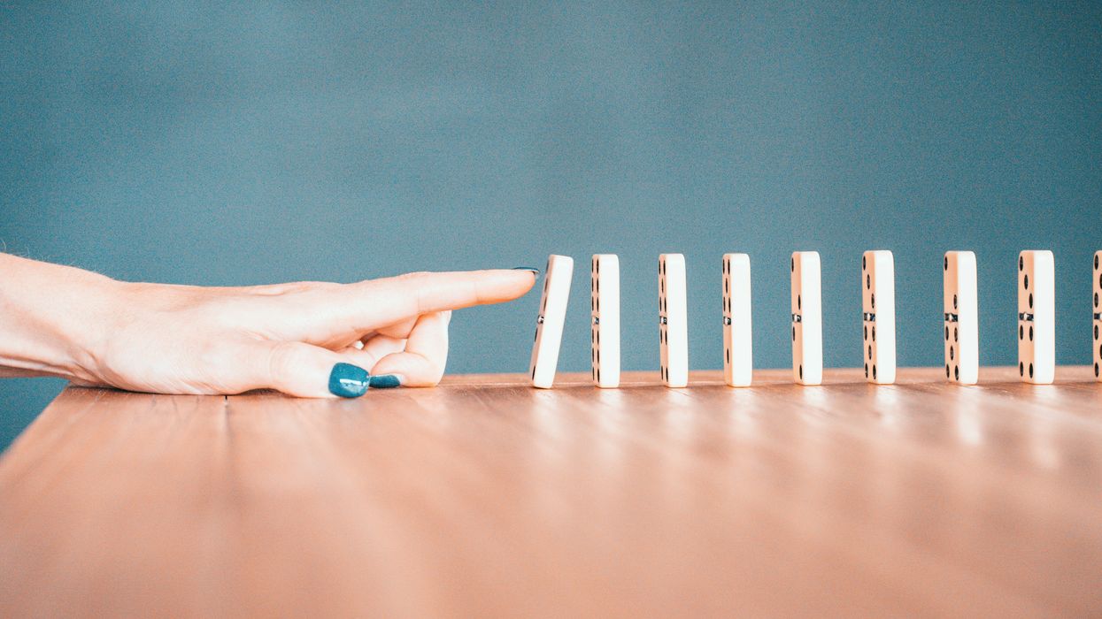 Person knocking over a row of dominoes