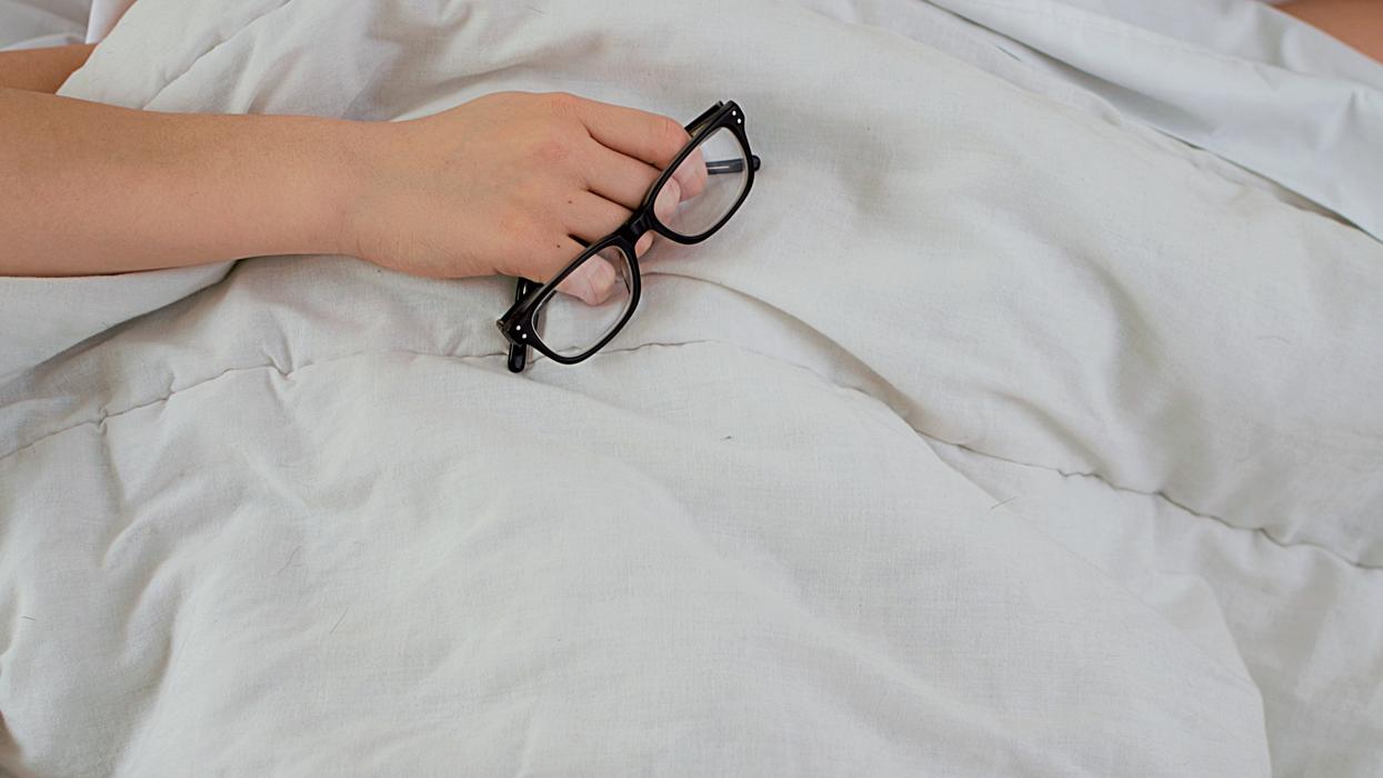 Person lying in bed with pillow covering their face