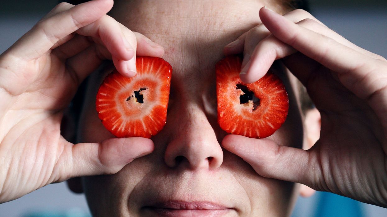 Person making a goofy face by holding slices of strawberry up to their eyes