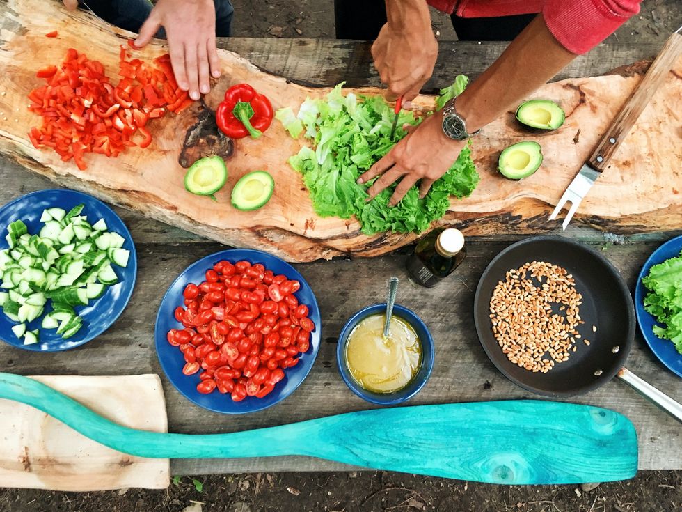 person slicing green vegetable in front of round ceramic plates with assorted sliced vegetables