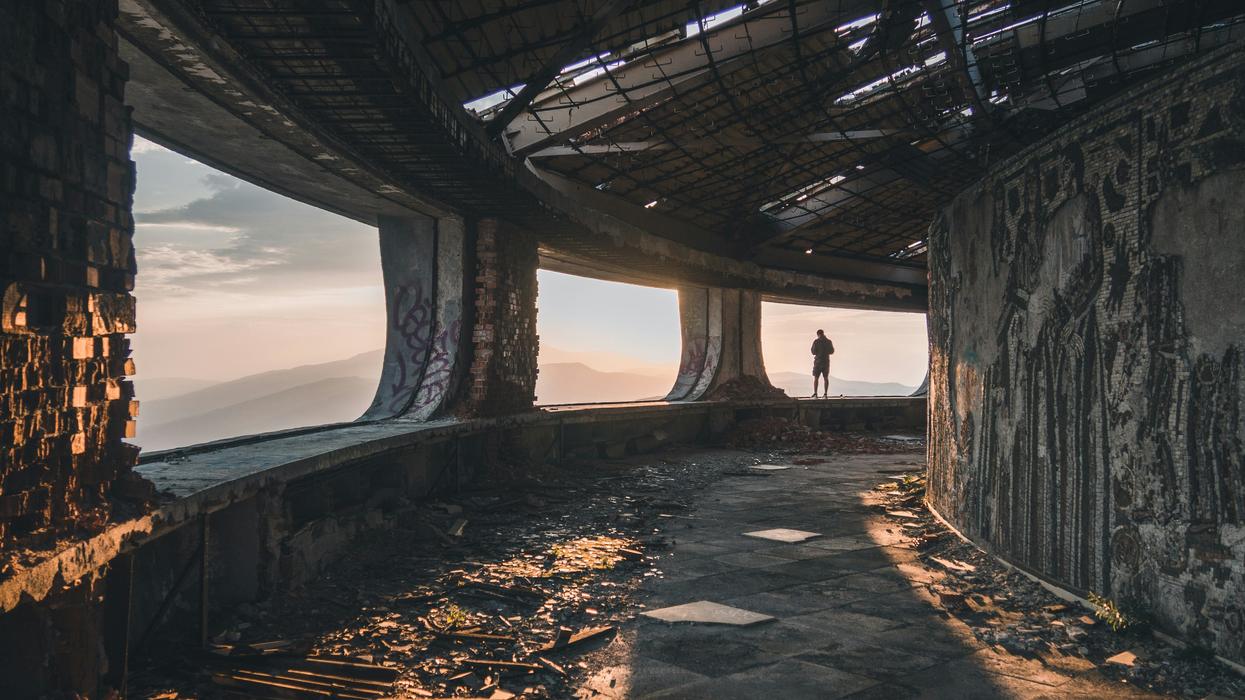 person standing on concrete beam facing mountain in Buzludzha, Bulgaria