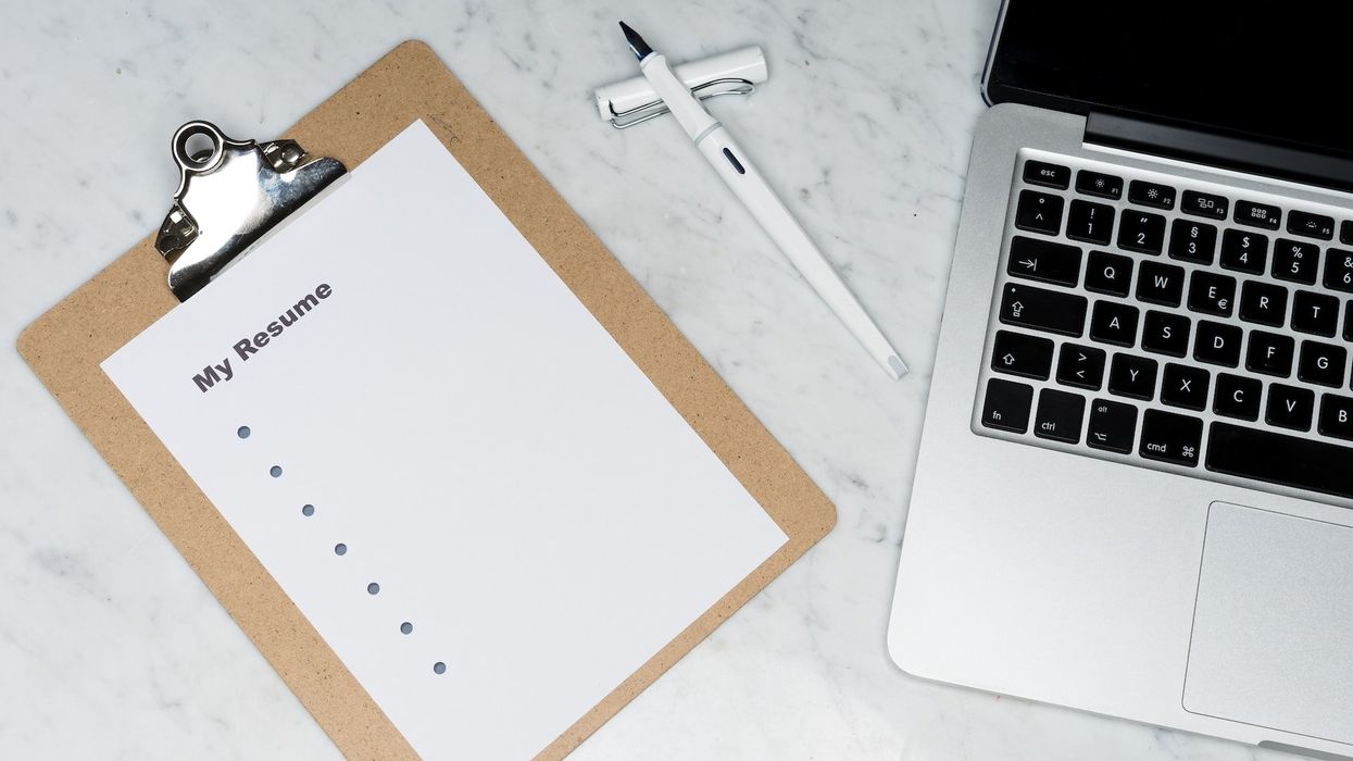 Photo of a clipboard with an empty resume, lying next to an Apple Macbook