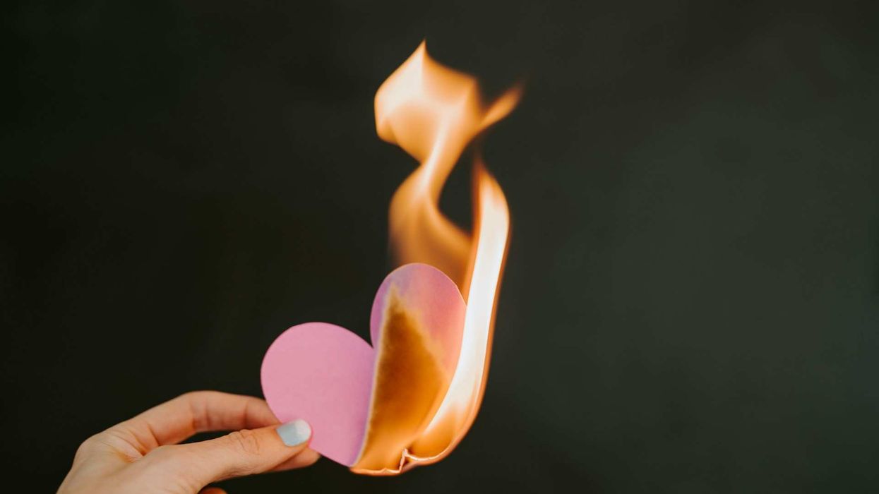 Photo of a female hand holding up a pink paper heart that is on fire.