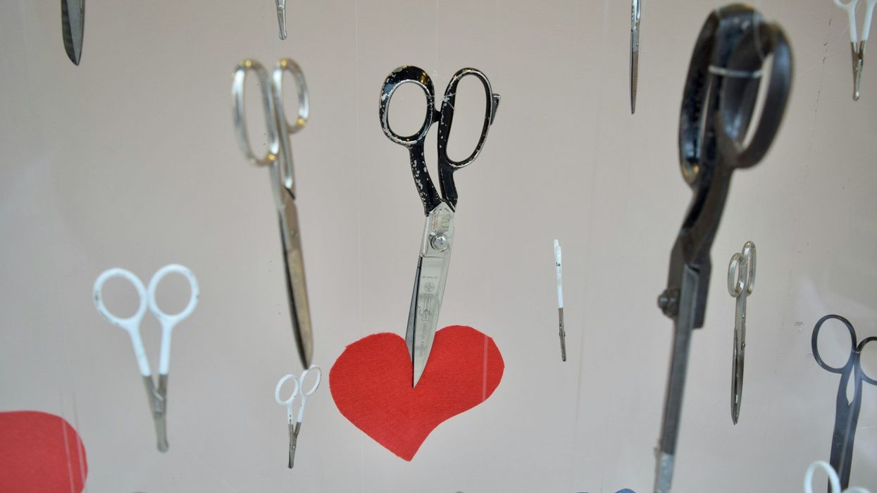 Photo of scissors raining down. One pair of shears captures a red paper heart.