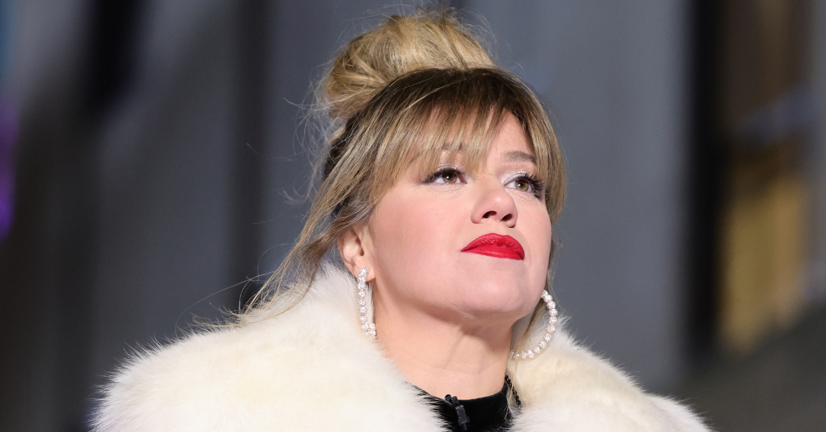 Photo of singer Kelly Clarkson. She is wearing a fluffy white jacket and large pearl hoop earrings.