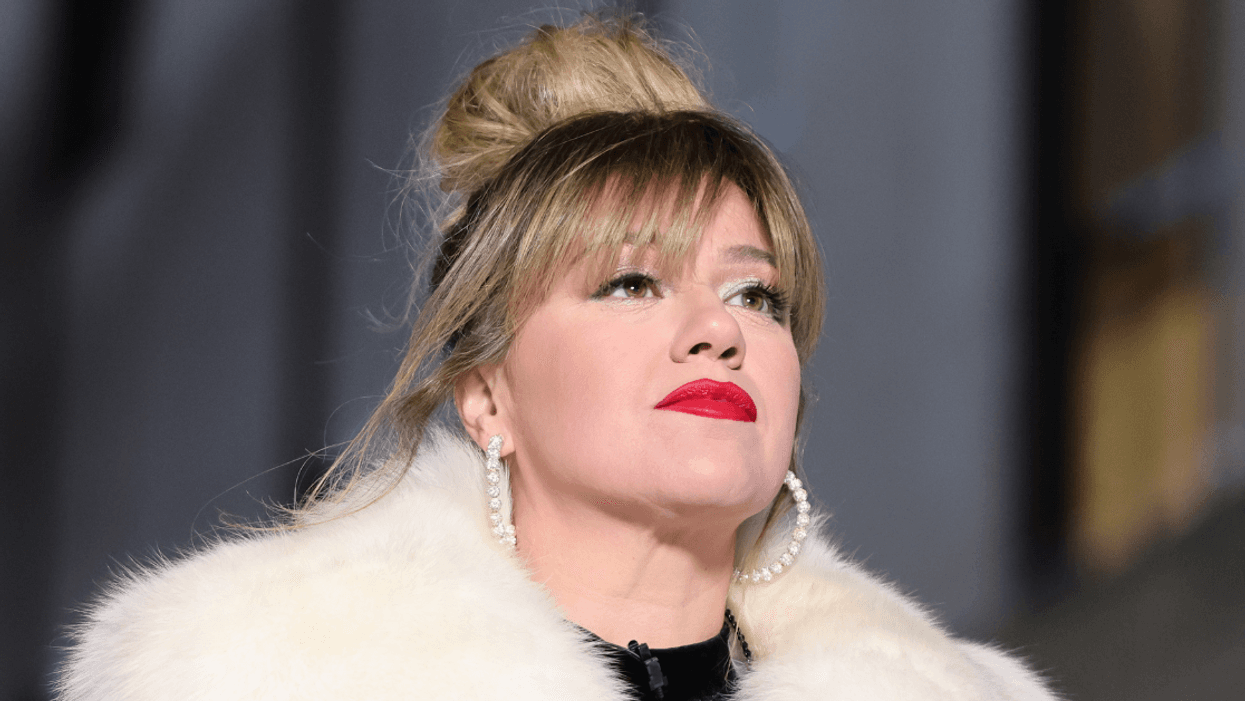 Photo of singer Kelly Clarkson. She is wearing a fluffy white jacket and large pearl hoop earrings.