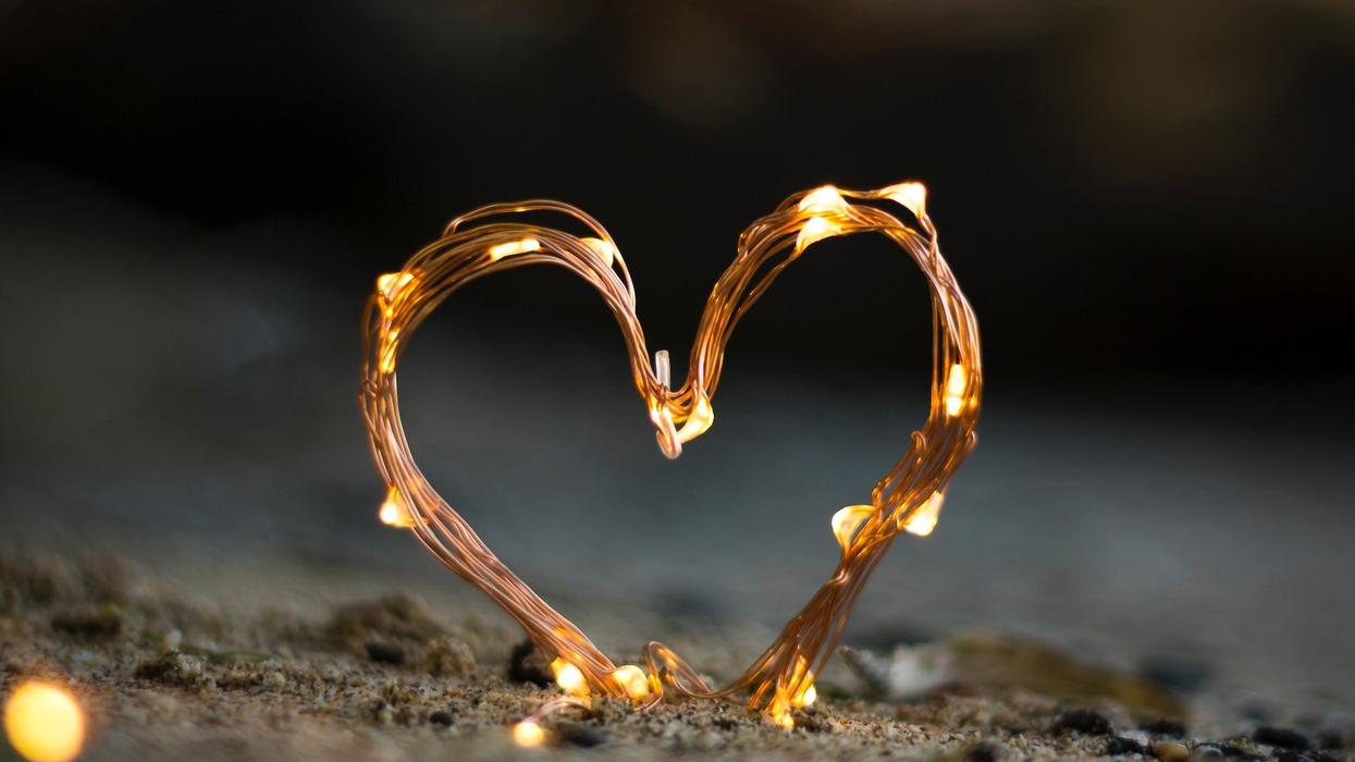 Picture of a heart constructed of wire and white lights and it sits on sand