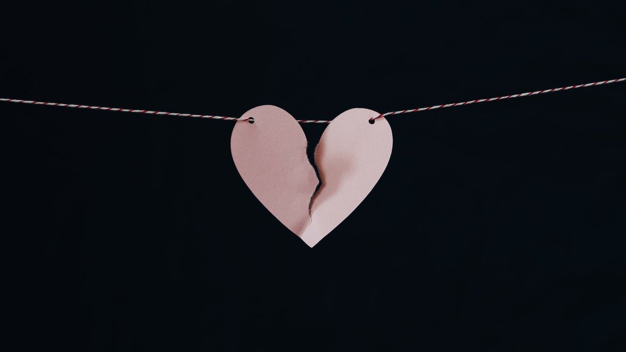 Picture of a pink heart tearing in two, hung off a red and white string, set against a black background