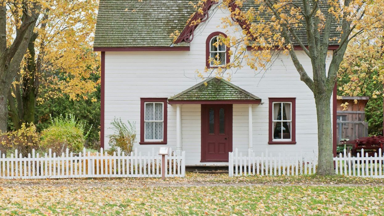 Picture of a traditional, American house. It is white with red trim and a green roof.