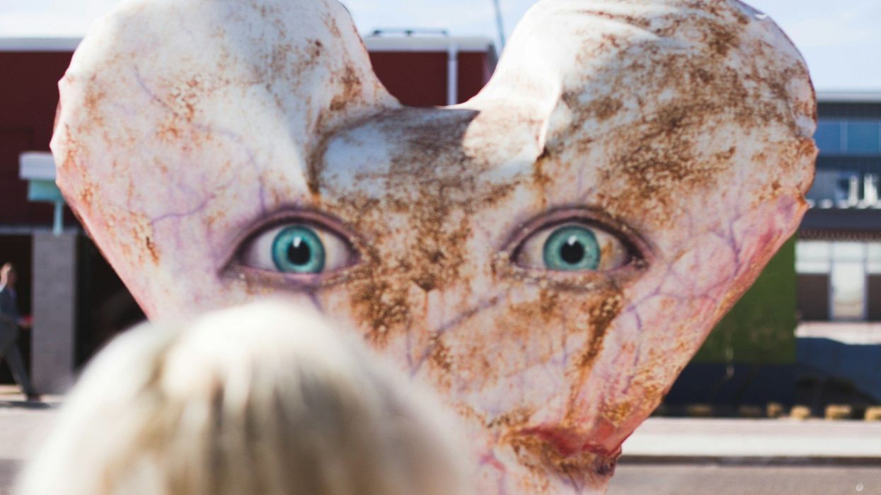 Picture of an artistic sculpture. It is a massive, rusted, white heart with blue eyes.