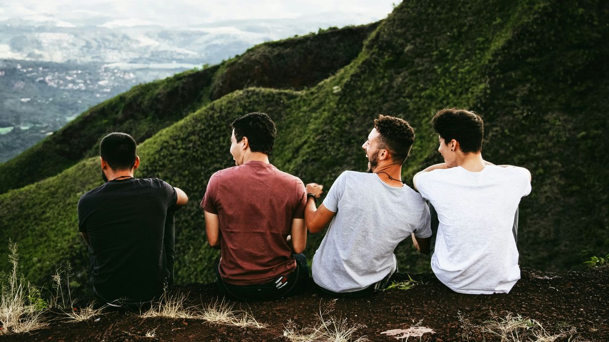 row of four men sitting on mountain trail