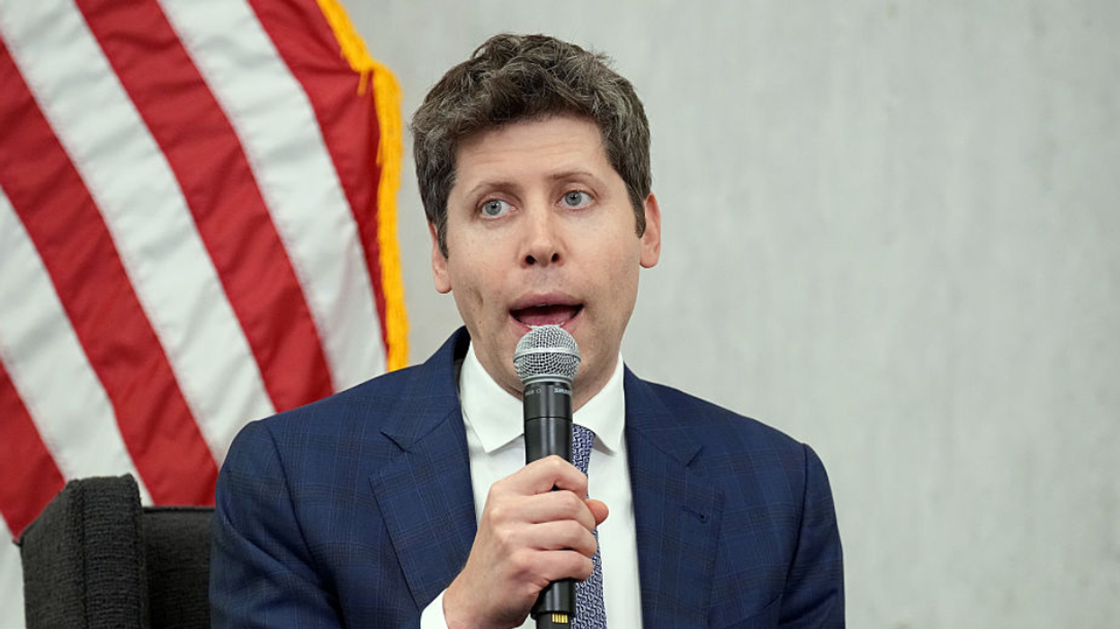 Sam Altman speaking into a microphone with an American Flag in the background.