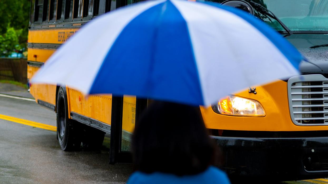 school bus greeted by parent with umbrella