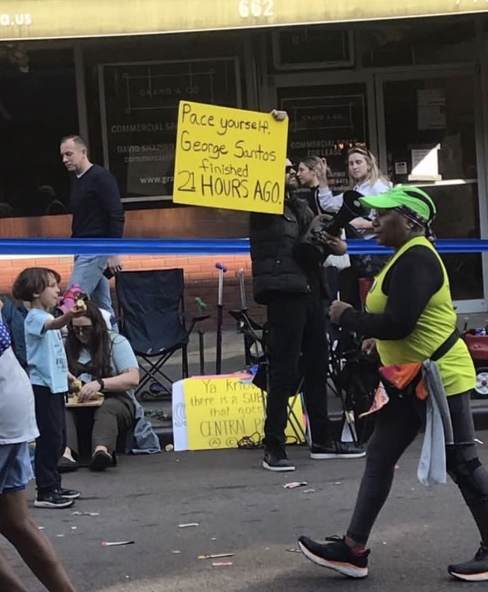Screenshot of individual holding sign mocking George Santos during the NYC Marathon