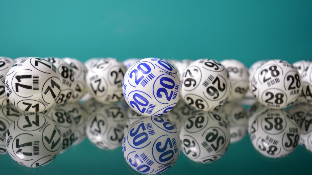 Several lotto balls lay on a mirrored floor; all the balls are white and black with different numbers except one that is white and blue, with the number 20