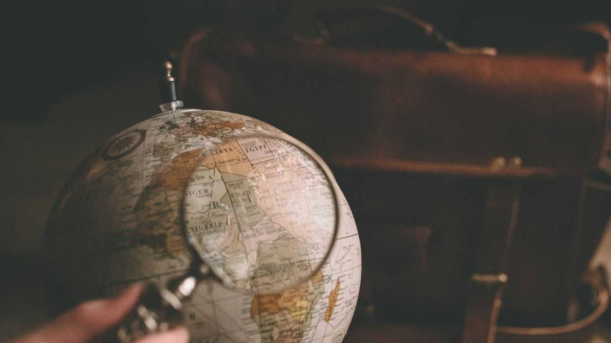 Shot of a hand holding a magnifying glass over a specific spot on a globe.
