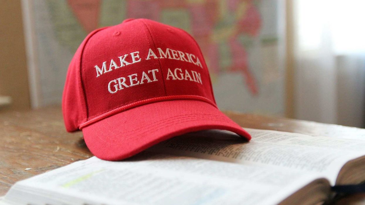Shot of a red 'MAGA' hat sitting on a dictionary, placed on a desk. A blurry map of the US is in the background.