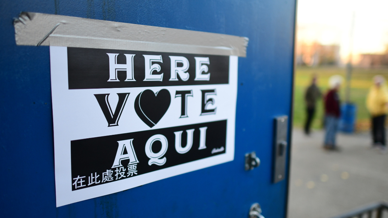 sign taped on blue door with "vote here" printed in multiple languages