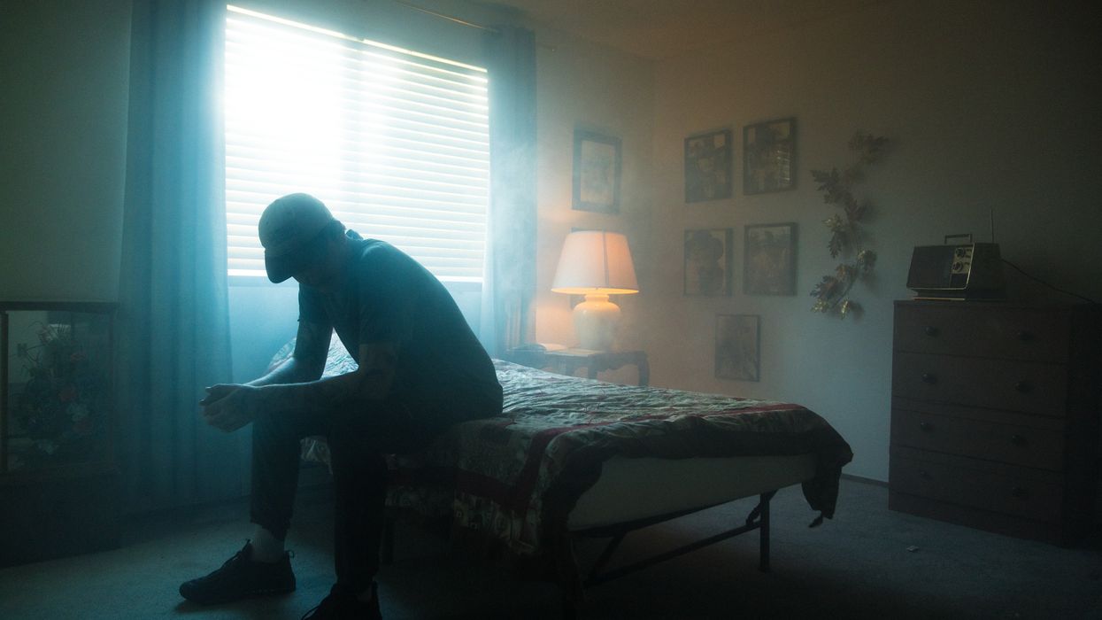 Silhouette of a man sitting on the edge of his bed looking down