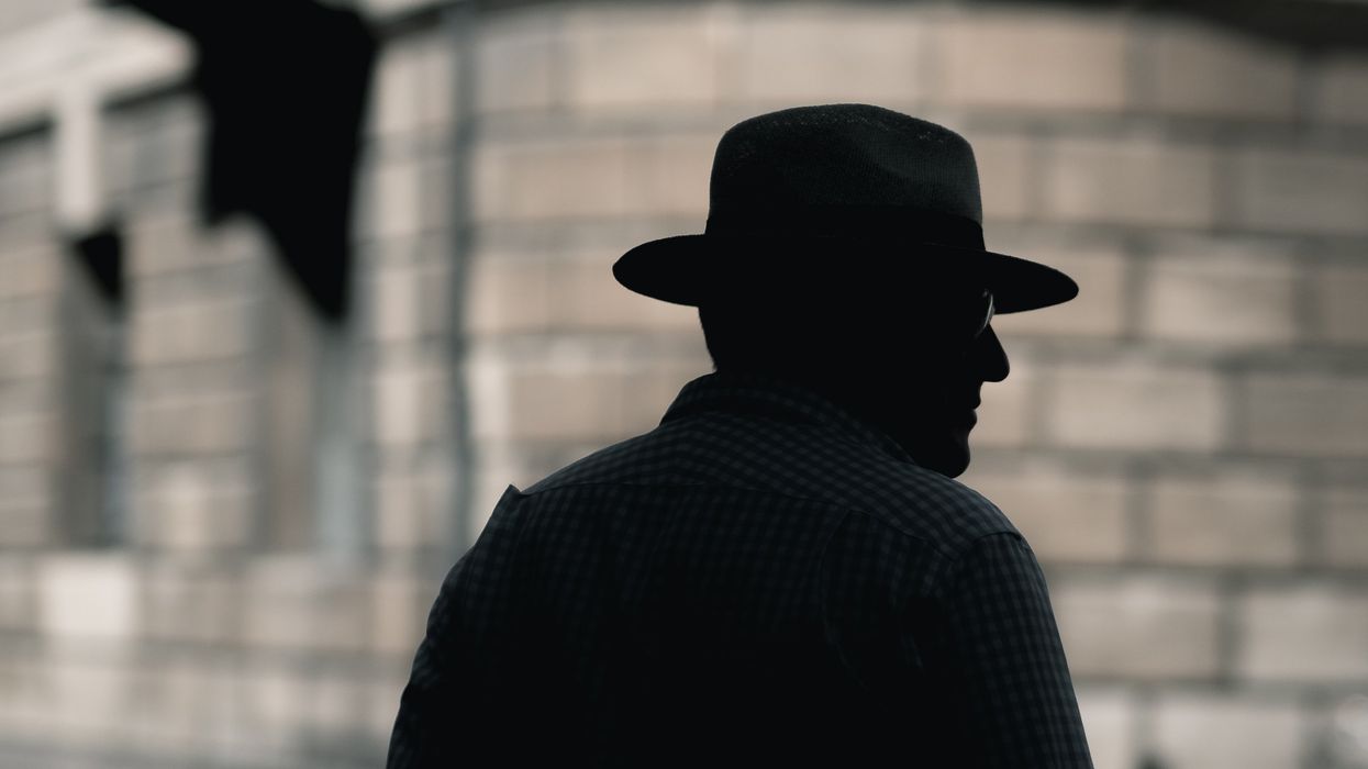 silhouette of a man with hat standing near concrete building in daytime