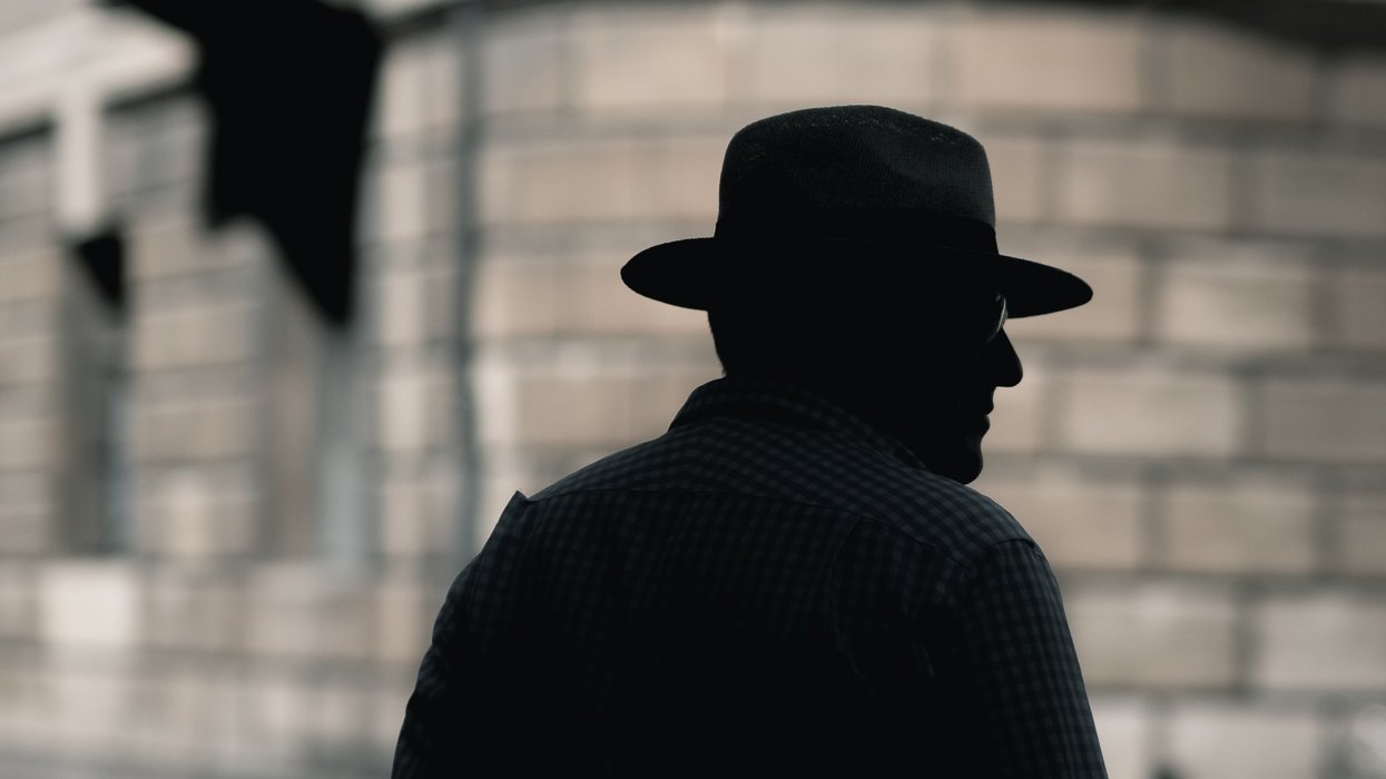 silhouette of a man with hat standing near concrete building in daytime