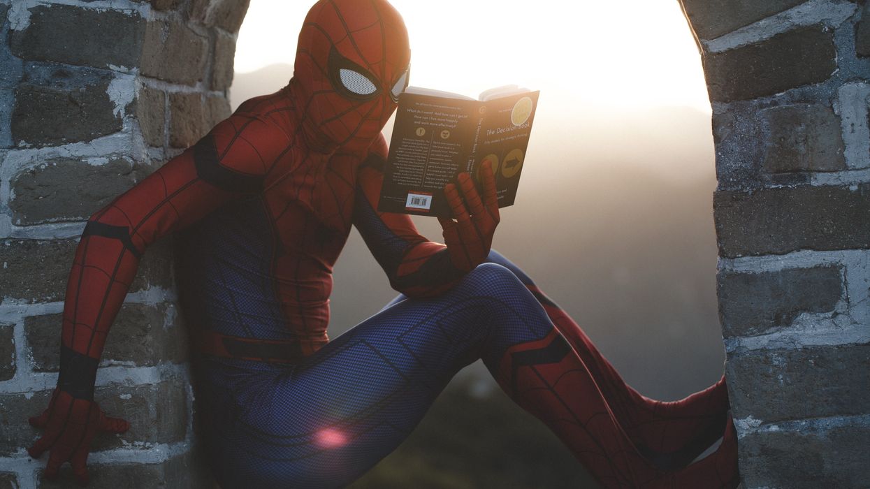 Spider-Man leaning on concrete brick while reading book