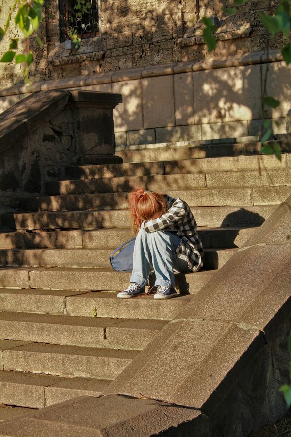 teen with face in arms sitting outside on concrete stairs
