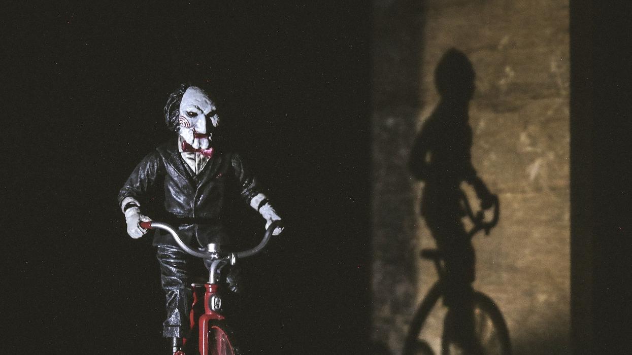 The frightening clown villain from SAW rides a red bike while their shadow follows