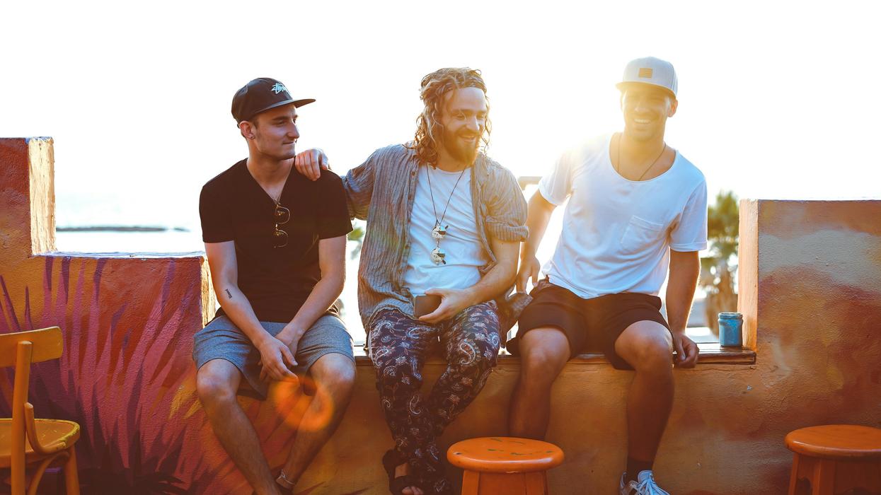 Three men sitting on a bench with the sun setting behind them.