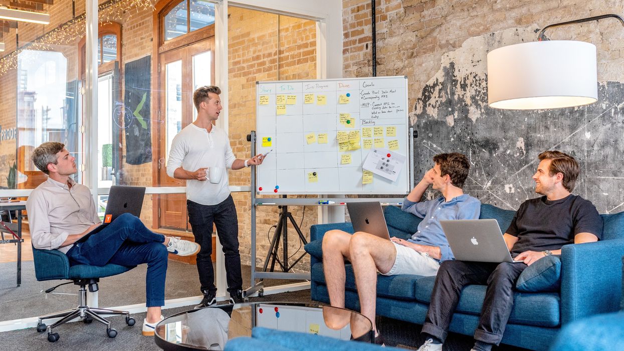 three men sitting while using laptops and watching man beside whiteboard