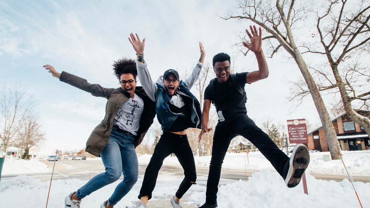 three people jumping on snowy path near bare trees