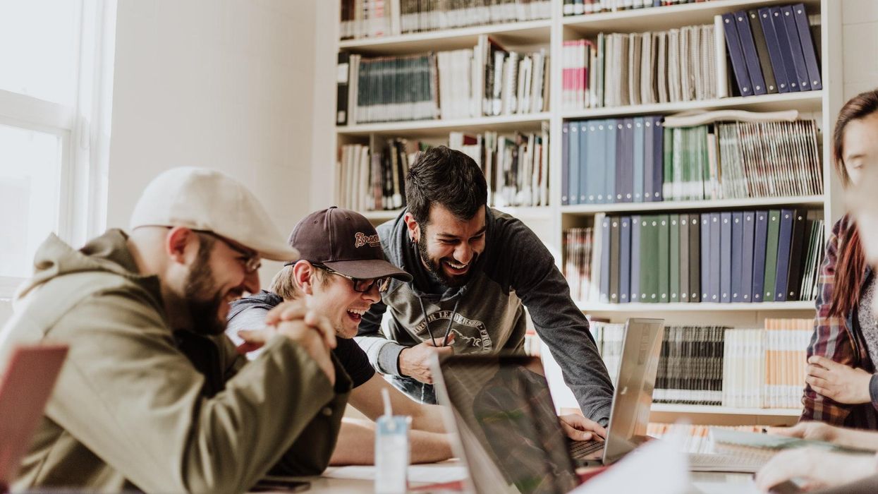 three young men at a table in a library looking at a laptop