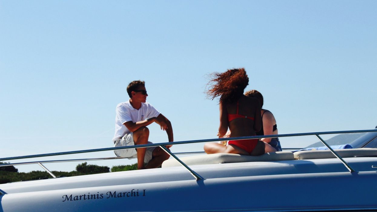 Three young people sit on the deck of a yacht on a beautiful day.