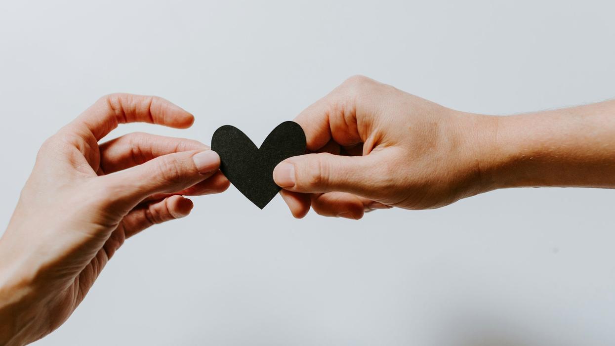 Two hands hold a black paper heart