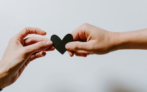 Two hands hold a black paper heart