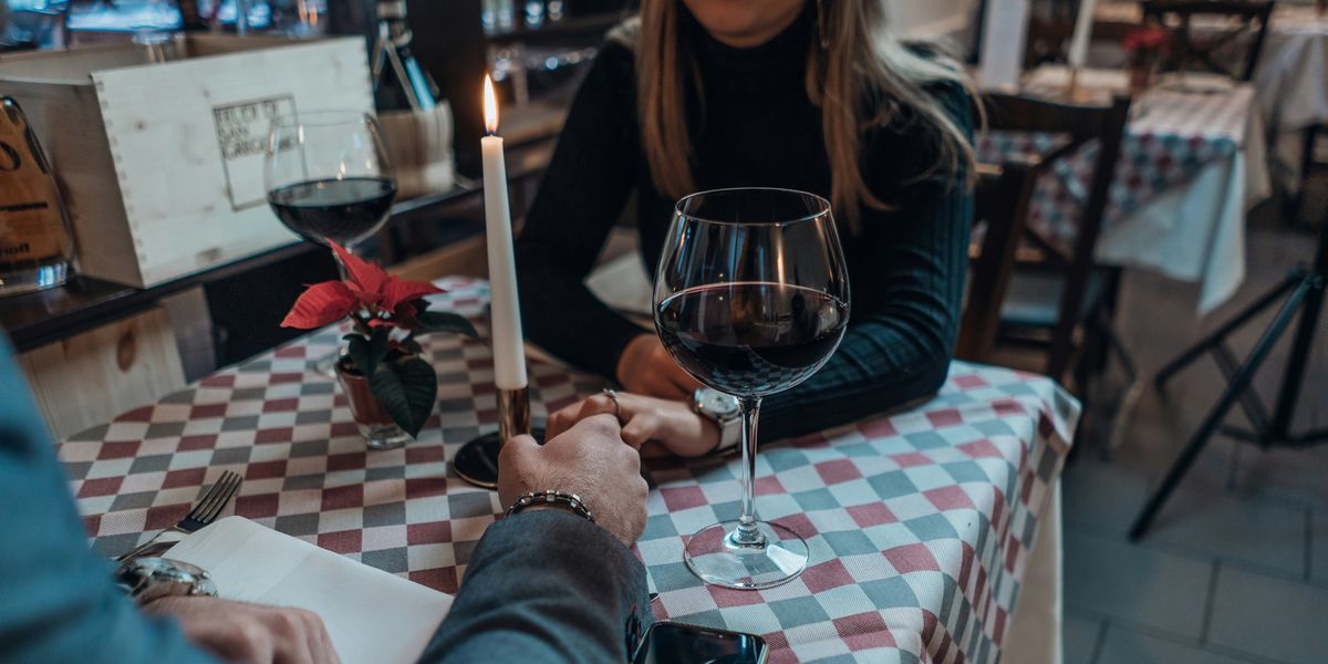 Two people holding hands across a table with with a glass of wine.