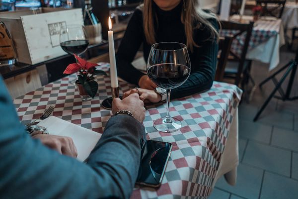 Two people holding hands across a table with with a glass of wine.