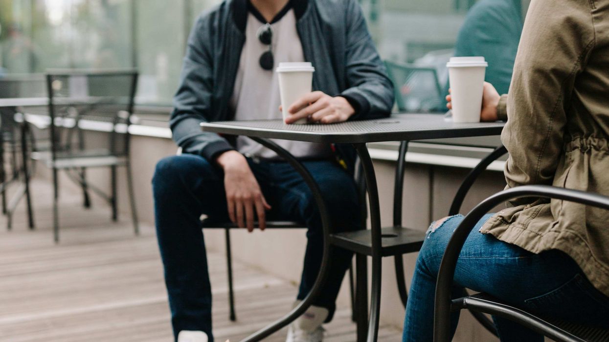 Two people sitting at an outdoor table with cups of coffee