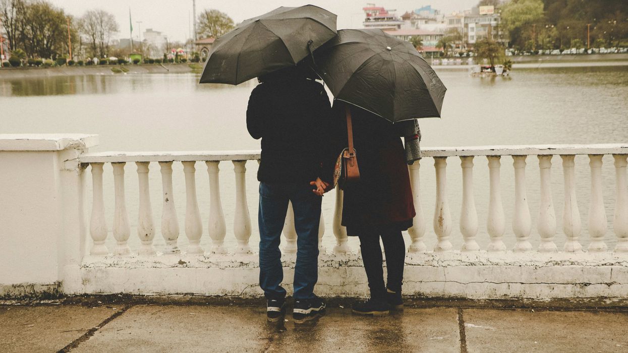 Two people standing next to each other on a bridge under black umbrellas