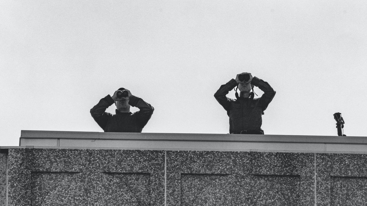 Two security people look out with binoculars from a roof
