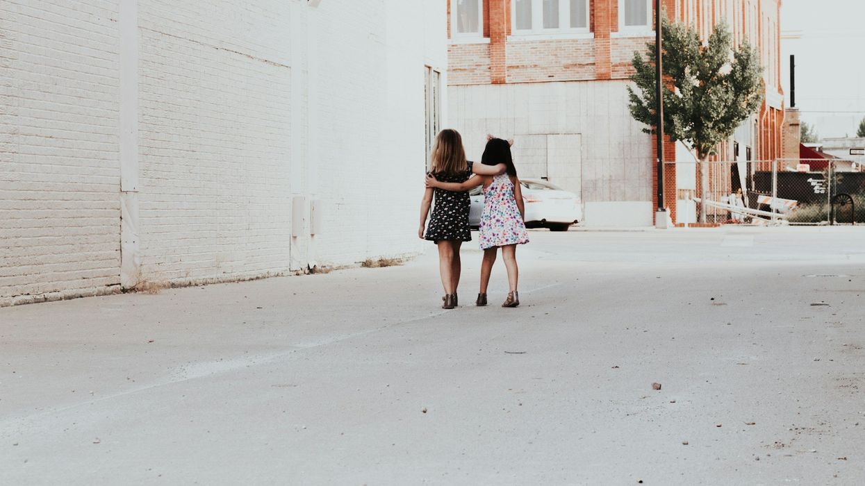 Two young girls walk away with their arms around one another