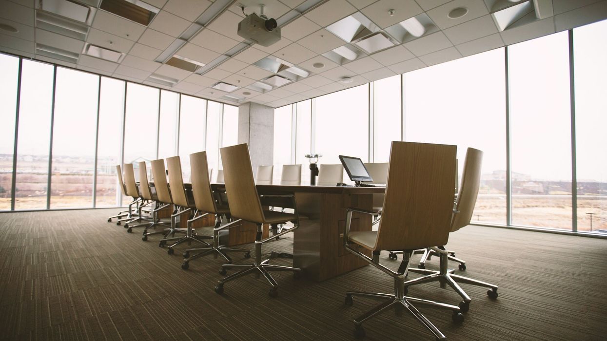 Wide shot of a boardroom with a wall of windows. There is a conference tables and many empty chairs.