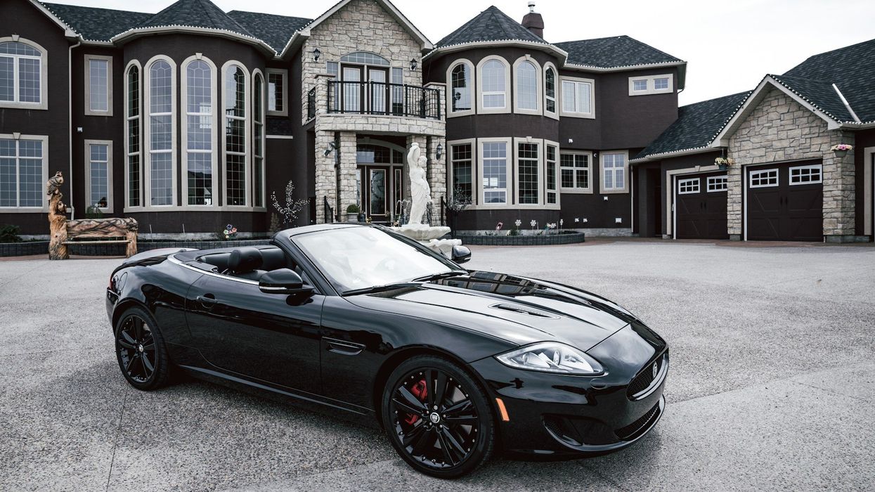 Wide shot of a mansion with fancy, black convertible parked out front.